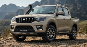 Front three-quarter view of the beige Mahindra Scorpio Lifestyler pickup truck on a rocky terrain with mountains in the background.